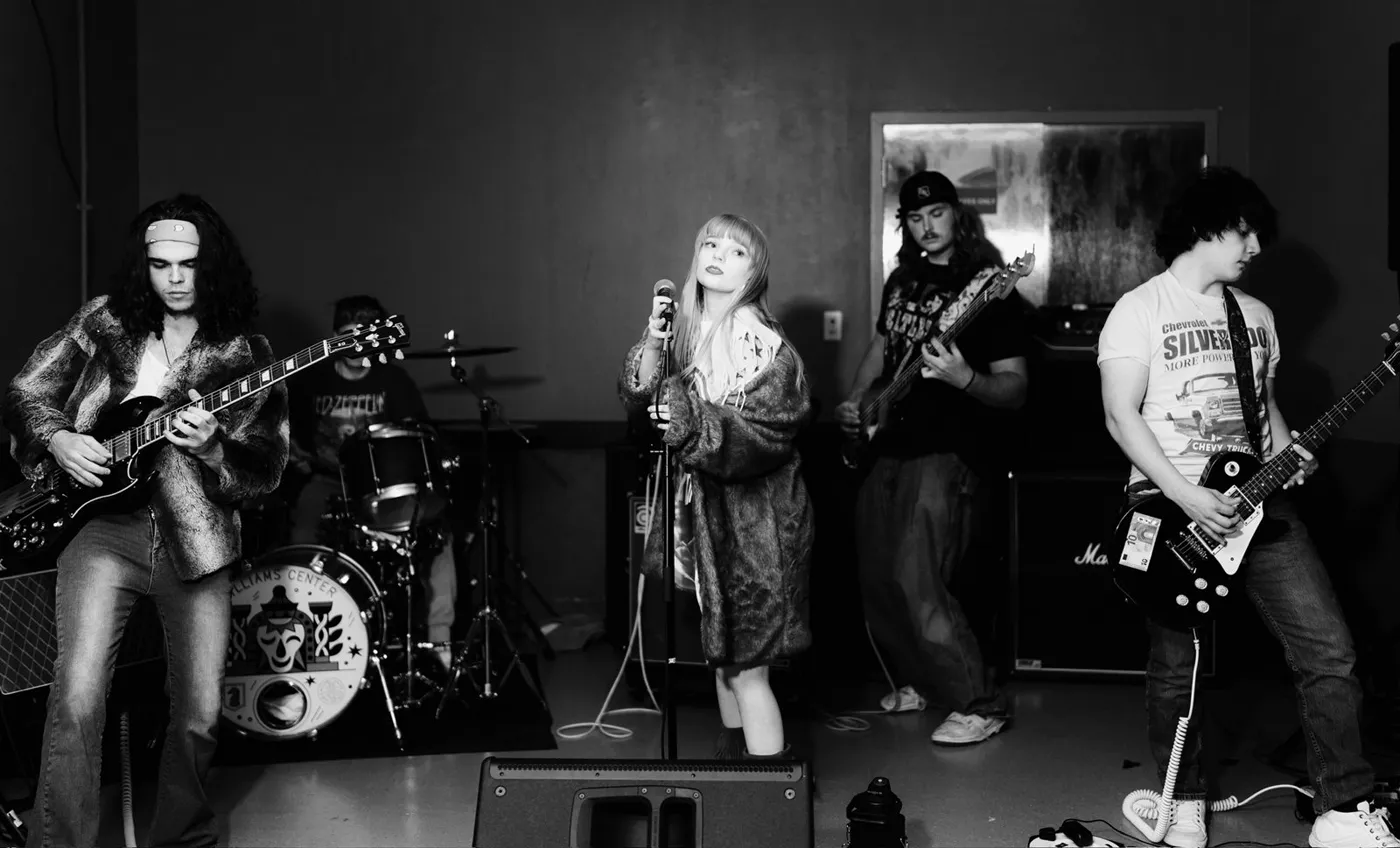 The five-piece in black and white on a low stage, the singer at the centre mic with a guitarist either side of her and the drummer behind, a doorway and a poster on the wall at the back